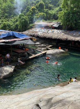 This image shows Elephant Springs (Suoi Voi) in Hue, Vietnam, a natural oasis with crystal-clear pools and large boulders surrounded by green foliage. Visitors can be seen enjoying a swim in the cool, refreshing waters or relaxing on the rocks. The area’s serene environment and unique features make it a popular destination for picnics, family outings, and nature lovers.