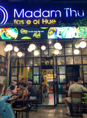 This image shows Madam Thu Restaurant, where the famous Bun Bo Hue is served. The image focuses on a steaming bowl of Bun Bo Hue, with tender beef and flavorful broth. The homey atmosphere of the restaurant is also visible, inviting guests for a relaxing and satisfying meal. The savory pancakes wrapped in rice paper are also featured, highlighting the variety and deliciousness of the traditional Vietnamese dishes offered at this cozy restaurant.