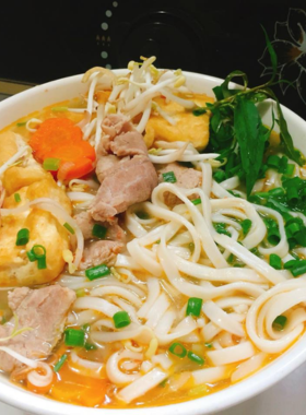 This image shows Bánh Canh Hue, a popular street food in Hue made with thick tapioca noodles served in a savory broth. The image focuses on a steaming bowl of Bánh Canh with fresh herbs and vegetables. It's a delicious and comforting dish, often enjoyed on the go while exploring the vibrant streets of Hue. The savory taste and satisfying texture make Bánh Canh a beloved dish for both locals and visitors alike, giving you a true taste of Hue’s culinary culture.