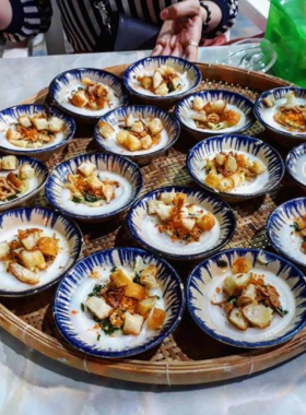 This image shows Bánh Bèo, a beloved street food in Hue. The picture highlights small steamed rice cakes topped with shrimp, fried shallots, and savory sauce. Bánh Bèo is a light, flavorful snack that can be enjoyed while strolling through Hue’s lively streets. It's a perfect example of the simple yet delicious food that Hue is known for, offering a delightful combination of textures and flavors in every bite.