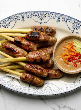 This image shows Nem Lui, a popular street food in Hue made from grilled minced pork skewers wrapped in rice paper with herbs. The image focuses on a skewer of Nem Lui served with a flavorful peanut dipping sauce. The smoky aroma and delicious taste make it a perfect snack or appetizer, popular at street food stalls around Hue. It's a great dish to enjoy while exploring the local markets or enjoying the lively atmosphere of Hue’s streets.