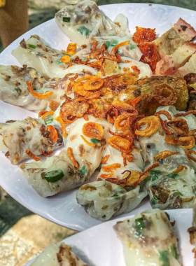 This image shows Bánh Tráng Cuốn, Vietnamese rice paper rolls filled with shrimp, pork, vegetables, and noodles. The image highlights the fresh rolls, served with a savory dipping sauce to enhance the flavors. Bánh Tráng Cuốn is a light and refreshing dish, perfect for a quick snack or light meal. The vibrant colors of the fresh ingredients make it an appealing and delicious choice for anyone looking to try traditional Vietnamese street food.