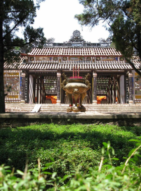 This image shows the serene gardens of Tu Hieu Pagoda, surrounded by tall pine trees and tranquil pathways. The pagoda, located in Hue, Vietnam, is a peaceful spiritual retreat with traditional Vietnamese architecture. The beautifully maintained garden reflects the calm and meditative atmosphere of the place, with small stone statues and lotus ponds adding to its charm. The image captures the cultural and spiritual essence of the pagoda, making it a must-visit destination for those seeking tranquility.