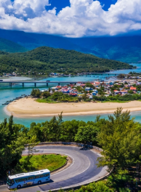 This image shows the golden sands of Lang Co Beach during sunset, with calm turquoise waves lapping against the shore. The sky is painted in vibrant hues of orange and pink, creating a magical atmosphere. The peaceful beach is surrounded by lush green mountains, making it a serene retreat near Hue, Vietnam. The image highlights the relaxing vibe of the beach, which is perfect for sunbathing, swimming, and enjoying fresh seafood from nearby local restaurants.