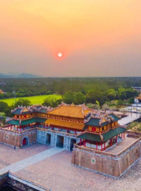 This image shows a local tour guide explaining Hue’s history to a small group of travelers near a historic site. The guide is pointing to an ancient structure while the visitors listen attentively. The scene is set against the backdrop of traditional Vietnamese architecture and lush greenery. The image highlights the engaging and educational experience of Hue Touring, where travelers can learn about the city’s rich culture, vibrant markets, and stunning landmarks through guided tours.