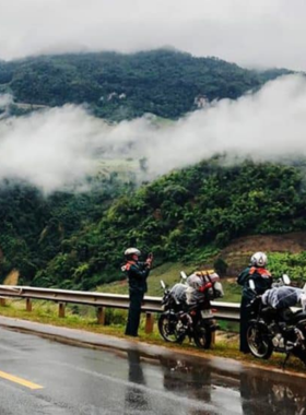 This image shows a motorbike rider cruising along the scenic Hai Van Pass, a popular route included in Hue Easy Rider tours. The road winds through green mountains with breathtaking views of the ocean on one side. The rider is equipped with a helmet and appears to be enjoying the adventure. The image captures the sense of freedom and excitement of exploring Hue and its surroundings on a motorbike, making it an ideal experience for thrill-seekers.