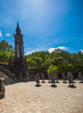 This image shows one of the Imperial Tombs of Hue, nestled in a tranquil setting surrounded by greenery and serene water features. The tomb’s intricate architecture is highlighted, with detailed carvings, colorful tiles, and grand archways. The peaceful atmosphere reflects the reverence for Vietnam’s emperors. Visitors can be seen walking along stone pathways, admiring the craftsmanship and learning about the historical significance of these royal resting places. The image captures the blend of art, culture, and history that defines these iconic tombs.