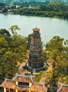 This image shows the Thien Mu Pagoda, Hue’s most iconic temple, perched on a hill overlooking the Perfume River. The seven-story structure stands tall, surrounded by lush greenery and vibrant flowers. Visitors are exploring the temple grounds, admiring the intricate carvings and historical artifacts. The peaceful river in the background adds to the serene atmosphere. The image reflects the spiritual and historical significance of this site, which offers a perfect blend of culture, tranquility, and stunning views of Hue’s landscape.