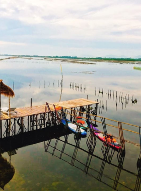 This image shows the breathtaking sunset view at Tam Giang Lagoon with vivid pink and orange hues in the sky. The tranquil water reflects the vibrant colors, creating a picturesque scene. Traditional fishing boats are floating peacefully, adding an authentic touch to the serene atmosphere. The surrounding wetlands are visible in the background, highlighting the natural beauty of this spot. The image captures the calm and relaxing vibe of Tam Giang Lagoon, ideal for nature lovers and photography enthusiasts.