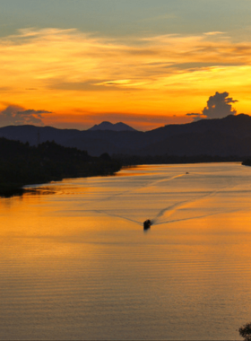 This image shows the panoramic view from Vong Canh Hill, overlooking the Perfume River and surrounding countryside. The lush green hills stretch into the distance under a clear blue sky. The river winds gently through the landscape, reflecting the natural beauty of the area. The peaceful vibe of the scene is perfect for a quiet retreat or capturing breathtaking photos. The image captures the essence of Vong Canh Hill as a serene and scenic destination in Hue.