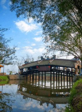 This image shows the Thanh Toan Tile Bridge, an iconic and historical structure surrounded by a serene rural village. The bridge’s intricate wooden design reflects Vietnam’s traditional architecture. Lush greenery and a calm waterway enhance the peaceful setting. A few locals can be seen nearby, adding life to the scene. The image highlights the charm and cultural significance of Thanh Toan Bridge, making it a perfect spot for exploring Hue’s heritage and capturing unique photos.