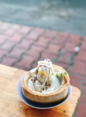 This image shows a refreshing coconut treat being served at Ben Tre Coconut in Da Nang. The image captures a customer enjoying chilled coconut water or creamy coconut jelly, offering a cool respite from the tropical heat. The cozy environment of the shop invites visitors to relax and unwind while indulging in these tropical delights. The lush greenery and simple décor enhance the relaxed vibe of the place.