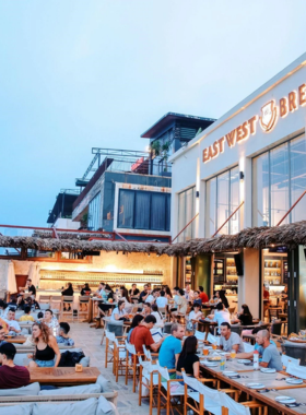 This image shows people enjoying craft beer at East West Brewing's beachfront taproom in Da Nang. The image captures the laid-back atmosphere with views of the beach, where visitors sip locally brewed pints and indulge in seafood dishes. The sound of the waves and the cool breeze add to the perfect ambiance. The image highlights the casual vibe of the beachside brewery, ideal for enjoying a drink with friends and great conversation.