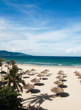 This image shows Non Nuoc Beach in Da Nang, Vietnam. The beach is known for its calm waters and long stretch of sandy shoreline. It’s less crowded compared to other beaches in the area, making it perfect for a relaxing day by the sea. The image showcases the peaceful beauty of Non Nuoc Beach, with people enjoying quiet walks along the shore or gently swimming in the cool, clear waters. The surrounding nature adds to the beach’s tranquility.