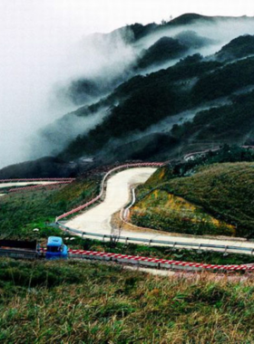 This image shows Hai Van Pass, a scenic mountain road that connects Da Nang and Hue in Vietnam. The winding road curves through lush green mountains, offering breathtaking views of the coastline and countryside. People can be seen stopping along the road to take photos or simply enjoy the panoramic views. The image showcases the beauty of the pass, with its steep turns and dramatic views, making it a popular destination for travelers seeking adventure and natural beauty.