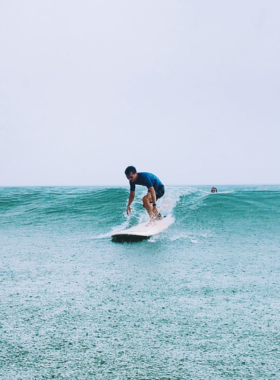 This image shows surfers riding the waves at My Khe Beach in Da Nang, Vietnam. The clear blue waters and consistent waves make it an ideal spot for surfing enthusiasts of all levels. The image highlights surfers enjoying the waves, with the beach and surrounding city in the background. My Khe Beach is popular for water sports, and the image captures the energy and thrill of surfing in this stunning coastal location.