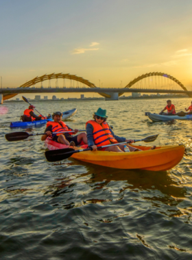 This image shows people kayaking in the calm waters of Tien Sa Beach in Da Nang, Vietnam. The image captures the peaceful atmosphere, with kayakers paddling through crystal-clear waters and enjoying the surrounding natural beauty. The beach offers a tranquil environment, making it a great place for water sports like kayaking. The surrounding hills and pristine shoreline provide a perfect setting for this relaxing water activity, ideal for both beginners and experienced paddlers.