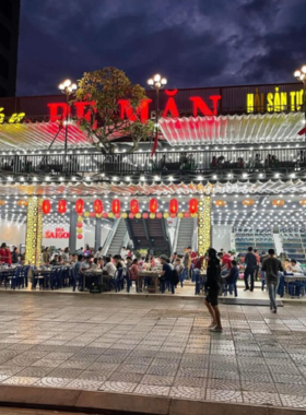 This image shows Hai San Be Man, a bustling seafood restaurant in Da Nang, known for its vibrant and casual atmosphere. The picture highlights fresh seafood being grilled and served, including lobsters, shrimp, and clams. Diners are seen enjoying their meals while soaking in the lively vibes near the beach. The simplicity of the seating and freshness of the dishes reflect the authentic charm of this restaurant.