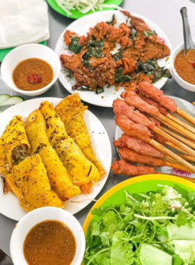 This image shows Banh Xeo Ba Duong, a popular street food stall in Da Nang specializing in Vietnamese pancakes, or banh xeo. The image captures the sizzling golden pancakes being freshly prepared on a hot skillet. Customers are seen enjoying their meals in a simple, casual seating area. The pancakes are served with fresh greens and dipping sauce, creating an authentic and flavorful dining experience.