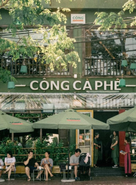 This image shows Cong Caphe, a vintage-themed café in Da Nang with military-inspired decor. The photo captures the nostalgic interiors featuring rustic furniture, old propaganda posters, and a cozy atmosphere. A glass of Vietnamese iced coffee with condensed milk is placed on the table, showcasing their iconic drink. Customers are seen enjoying the laid-back vibe while chatting or reading. The unique theme and creative drinks make this café a memorable experience.