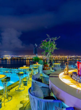 This image shows Sevva Sky Lounge, a sophisticated rooftop bar in Da Nang offering incredible views of the city. The bar features a stylish design with cozy seating areas, mood lighting, and an elegant ambiance. Guests are seen sipping on cocktails and enjoying the serene yet upscale atmosphere. The breathtaking city skyline adds to the charm, making Sevva Sky Lounge an ideal destination for romantic evenings or chic gatherings.