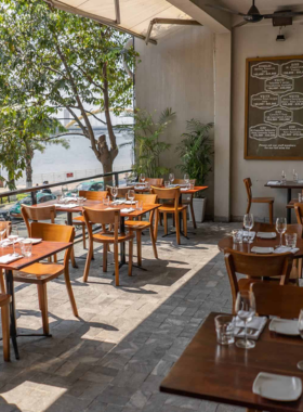 This image shows Waterfront Da Nang, a scenic riverside bar along the Han River. The view from the bar showcases the serene water and the city lights reflecting on the surface. Guests are seen enjoying cocktails on an open terrace, surrounded by soft lighting and relaxed decor. The peaceful atmosphere makes it a favorite spot for unwinding, especially during sunset, offering both locals and visitors a tranquil yet stylish nightlife experience.