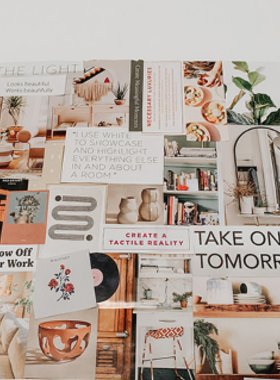 This image shows a person sitting at a desk covered with magazines, scissors, glue, and colorful paper. A partially completed vision board is visible, featuring cut-out images, quotes, and creative decorations. The person is actively cutting out another image, symbolizing the process of visualizing goals and aspirations. The background includes motivational posters and a small potted plant, creating an inspiring workspace for crafting a vision board filled with dreams.