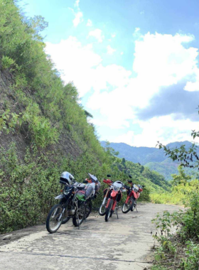 This image shows a motorbike rider exploring the lush green rice fields of Hoi An. A narrow dirt path cuts through the fields, leading to a scenic countryside dotted with small homes and palm trees. The rider is surrounded by endless greenery under a bright blue sky. This adventure offers visitors the chance to connect with nature, meet friendly locals, and discover the hidden gems of Hoi An’s rural areas.