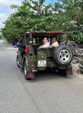 This image shows a vintage jeep traversing the winding mountain roads during the Tribee Adventure Jeep Tour. The scene highlights breathtaking views of lush green valleys and rugged hills under a bright blue sky. The passengers are smiling and enjoying the open-air ride, while the guide explains the significance of the surrounding landmarks. This thrilling off-road adventure combines stunning scenery, historical insights, and cultural exploration, offering a unique way to experience Vietnam’s countryside in a single day.