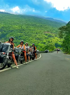 This image shows a group of motorbike riders exploring the picturesque countryside of Hoi An. The scene features lush green fields, winding dirt paths, and distant mountains under a clear sky. Riders are smiling as they pass by small traditional homes and waving locals, enjoying the off-the-beaten-path experience. The tour showcases quiet beaches, historic landmarks, and hidden gems, providing a perfect mix of adventure, culture, and scenic beauty. It’s an ideal activity for those seeking to uncover Hoi An’s true charm.