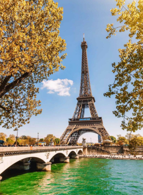 This image shows the iconic Eiffel Tower standing tall over the Paris skyline, showcasing its impressive iron structure. The photo captures the tower from a distance, with the lush greenery surrounding the Champ de Mars park below. The Eiffel Tower is one of the most famous landmarks in the world, attracting millions of visitors annually. It offers breathtaking views of Paris from the top, making it a must-see for any traveler in the city.