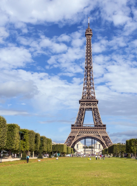 This image shows the iconic Eiffel Tower in Paris, France, a stunning iron structure standing tall against the backdrop of the city. The surrounding Champ de Mars gardens are lush and inviting, perfect for picnics and relaxation. The Eiffel Tower is beautifully illuminated at night, sparkling with lights and attracting visitors from around the world to enjoy panoramic views of Paris.