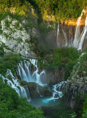 This image shows cascading waterfalls and turquoise lakes at Plitvice Lakes National Park in Croatia. Wooden trails wind through lush greenery, allowing visitors to walk over crystal-clear waters and enjoy panoramic views of this UNESCO World Heritage site. The vibrant natural beauty of the park is a haven for nature lovers and photographers.