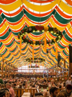 This image shows the lively Oktoberfest festival in Munich, Germany, with people dressed in traditional dirndls and lederhosen. Large beer tents are filled with cheerful crowds enjoying pretzels, mugs of beer, and Bavarian music. The festive atmosphere is vibrant and welcoming, showcasing Bavarian culture at its best.