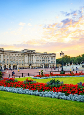 This image shows the Changing of the Guard ceremony at Buckingham Palace in London, England. Guards dressed in iconic red uniforms and bearskin hats march in formation to the sound of live music. The grandeur of the palace provides a regal backdrop, as spectators gather to witness this time-honored tradition.