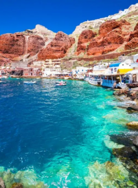 This image shows the unique beaches of Santorini, Greece, with black and red sands set against a stunning backdrop of whitewashed buildings and the Aegean Sea. Visitors relax under umbrellas, swim in clear waters, and enjoy fresh seafood at nearby taverns. The dramatic cliffs and serene vibe make Santorini a perfect getaway.