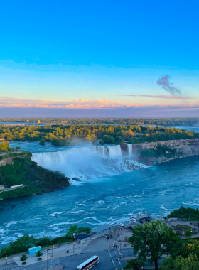 This image shows the powerful Niagara Falls, one of the world's most famous waterfalls, located on the border of Canada and the USA. The massive waterfall sends millions of liters of water crashing down every second, creating a misty atmosphere. The scenic viewpoint allows visitors to witness the falls up close, with a rainbow often forming over the rushing water. Boat tours like the Maid of the Mist take visitors closer to the falls, offering an unforgettable experience. The surrounding area is filled with attractions, restaurants, and walking trails.