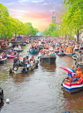 This image shows a crowd of people dressed in orange celebrating King’s Day in the Netherlands, the country’s national holiday. The day is marked with street parties, music festivals, flea markets, and an overall joyful atmosphere. King’s Day celebrates the Dutch royal family, and citizens nationwide wear orange, the color of the royal family, to honor the occasion. The image captures the energy and excitement of the festivities, with people of all ages joining in the fun.