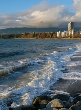 This image shows English Bay Beach, a beautiful and relaxing waterfront destination in Vancouver. People are sunbathing on the sandy shore, while others are swimming or kayaking in the calm ocean waters. The city skyline and mountains create a breathtaking backdrop. Some visitors are sitting at beachside cafés, while others are enjoying a peaceful sunset walk along the waterfront. It’s the perfect spot for unwinding, picnicking, and soaking in Vancouver’s stunning coastal views.