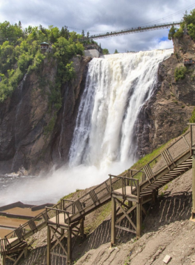 This image shows the breathtaking Montmorency Falls, one of the tallest waterfalls in Canada, located just outside Quebec City. The falls are surrounded by lush greenery and offer a dramatic view as the water cascades down into the river below. In winter, the falls freeze into a stunning ice formation. Montmorency Falls is a natural wonder that visitors can admire from various viewing platforms and even walk across the suspension bridge.