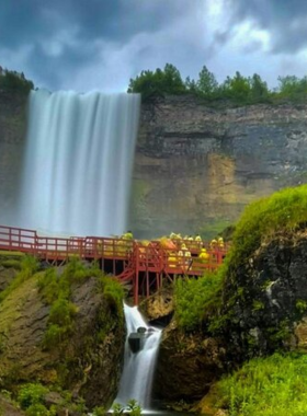 This image shows visitors walking along the wooden platforms of the Cave of the Winds, standing just a few feet away from the Bridal Veil Falls. Tourists are wearing yellow ponchos to shield themselves from the powerful waterfall spray. The walkway is surrounded by lush greenery and rocks, and the thunderous sound of water crashing down fills the air, offering an up-close and immersive experience of the falls like no other.