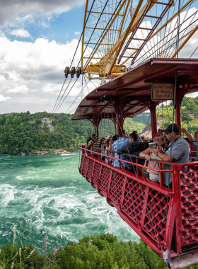 This image shows the Whirlpool Aero Car floating above the Niagara Whirlpool, offering passengers breathtaking views of the powerful swirling waters below. The red cable car is gliding over the river, providing an aerial view of the region’s dramatic landscape. The surrounding lush greenery and the majestic Whirlpool make this experience feel both thrilling and serene, giving a unique perspective of Niagara Falls.