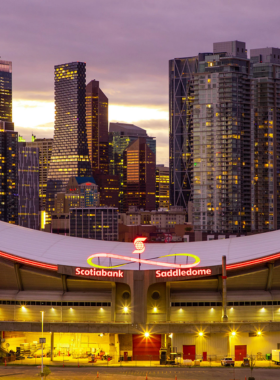 This image shows the excitement of a Calgary Flames hockey game at the Saddledome, where fans cheer on their team with energy and enthusiasm. The Saddledome is a premier venue for sports events, particularly hockey, and offers an electrifying atmosphere for live games. Fans from all over gather to witness the fast-paced action on the ice, creating a thrilling experience for sports lovers and newcomers alike, especially during the hockey season when the Flames are playing their best.