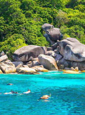 This image shows Hin Wong Bay in Koh Tao, a quiet and secluded spot famous for snorkeling. The bay is surrounded by rugged cliffs and dense vegetation, with crystal-clear waters teeming with vibrant coral reefs and diverse marine species. It is an ideal destination for adventure lovers seeking an untouched snorkeling experience.