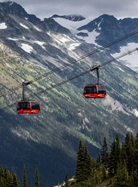 This image shows the Peak 2 Peak Gondola suspended high above the mountains, offering a spectacular panoramic view of Whistler and Blackcomb. The glass cabin provides a breathtaking look at the surrounding peaks, valleys, and dense evergreen forests. Visitors inside the gondola admire the stunning landscape, taking pictures of the incredible scenery. The bright blue sky and snow-covered mountains create a picturesque backdrop, making this an unforgettable experience for travelers in Whistler.