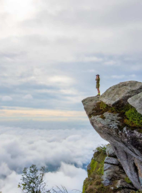 This image shows hikers on the trail leading to Khao Phra Mae Ya in Sukhothai, with picturesque views of dense forests and the majestic Khao Luang Peak, offering an adventure through nature’s wonders.