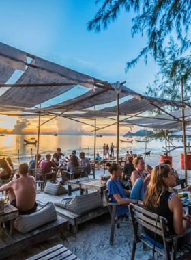 This image shows Blue Water Cafe, a relaxed cafe and bar with an ocean view. It's the perfect place to enjoy delicious international and Thai dishes, refreshing drinks, and live music while watching a beautiful sunset.