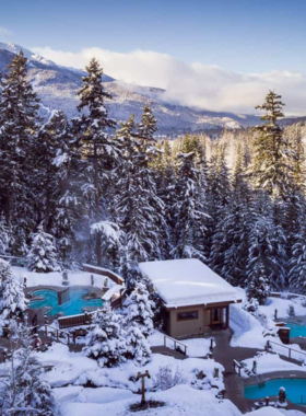 This image shows the peaceful setting of Scandinave Spa in Whistler, with steaming hot pools surrounded by snow-covered trees. Visitors relax in the warm water while enjoying the quiet forest ambiance. The wooden architecture and stone pathways enhance the natural beauty of the spa. This image captures the essence of relaxation, offering a glimpse into the rejuvenating experience of soaking in hot pools amidst a serene winter landscape.