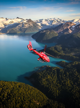 This image shows an aerial view of Whistler’s majestic mountains, glaciers, and alpine lakes, as seen from a helicopter. The helicopter soars high above, offering breathtaking panoramic views of the rugged landscape below. The blue sky contrasts with the white snow and deep green forests, creating a stunning natural tapestry. This image captures the excitement and beauty of experiencing Whistler from the sky on a thrilling helicopter tour.