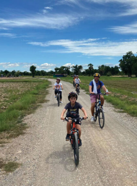 This image shows tourists cycling through the peaceful countryside of Sukhothai, passing by rice paddies and rural villages, offering a calm yet adventurous way to experience the natural beauty and local culture.